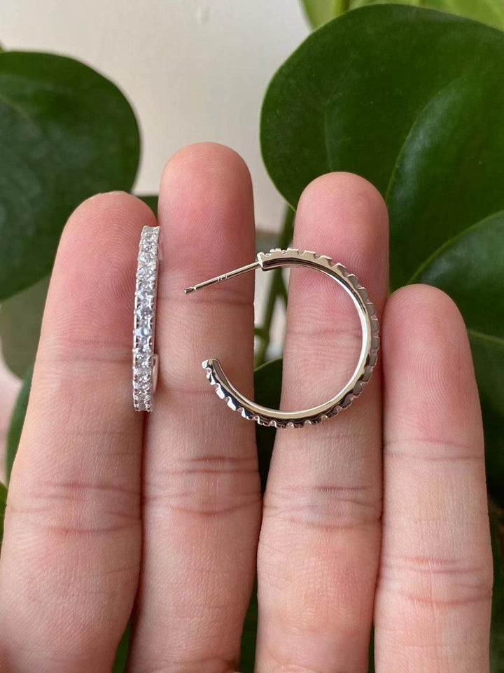 A pair of silver-colored earrings with one featuring a crystal-embellished bar and the other a classic hoop design, held in a person's hand.