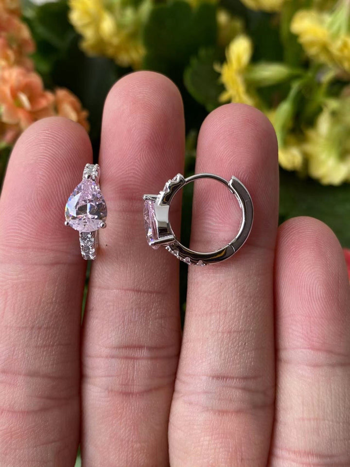 A pair of silver-colored hoop earrings with cubic zirconia displayed on a person's fingertip.