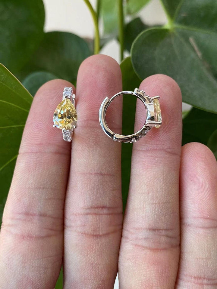A pair of silver-tone hoop earrings with green crystal accents, held in a person's hand.