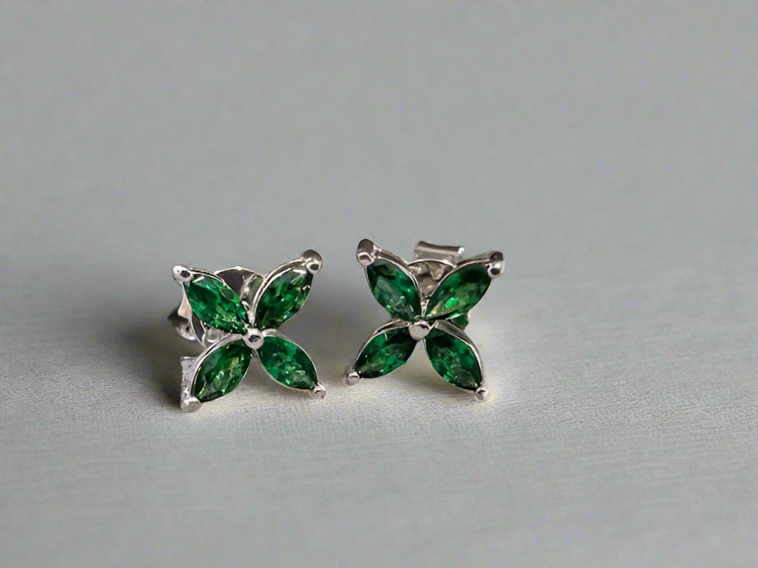 Butterfly-shaped earrings with green gemstones on a textured gray background
