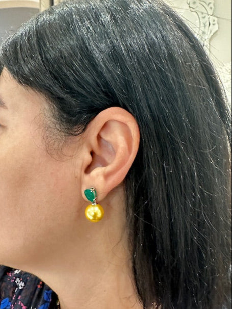 Close-up of an ear wearing a yellow earring with a green gemstone.