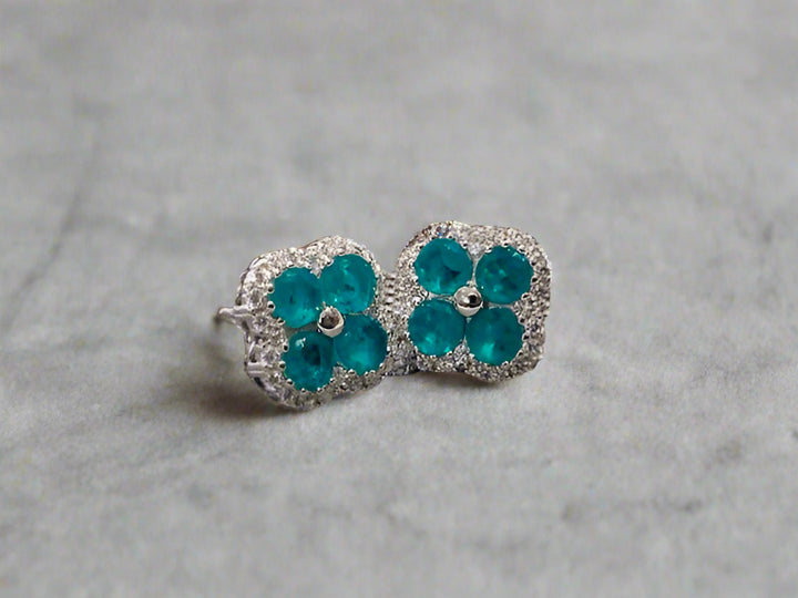 Pair of teal flower-shaped earrings on a textured surface